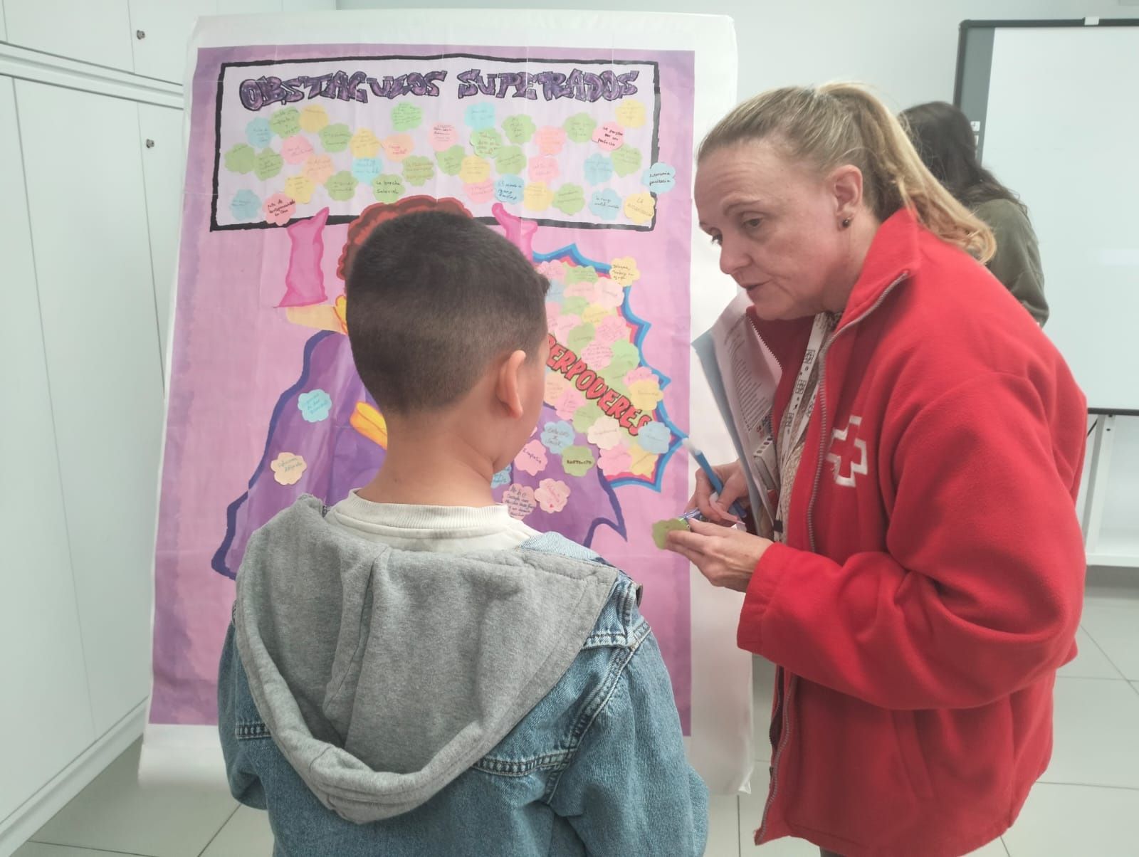 Una responsable de Cruz Roja colabora con un niño en la ejecución de una de las actividades del taller