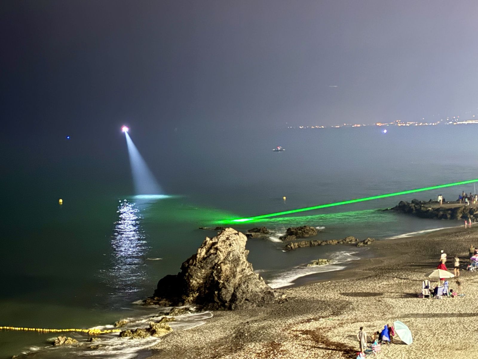 El foco blanco del dron y la luz verde del láser marcando la posición de los nadadores.