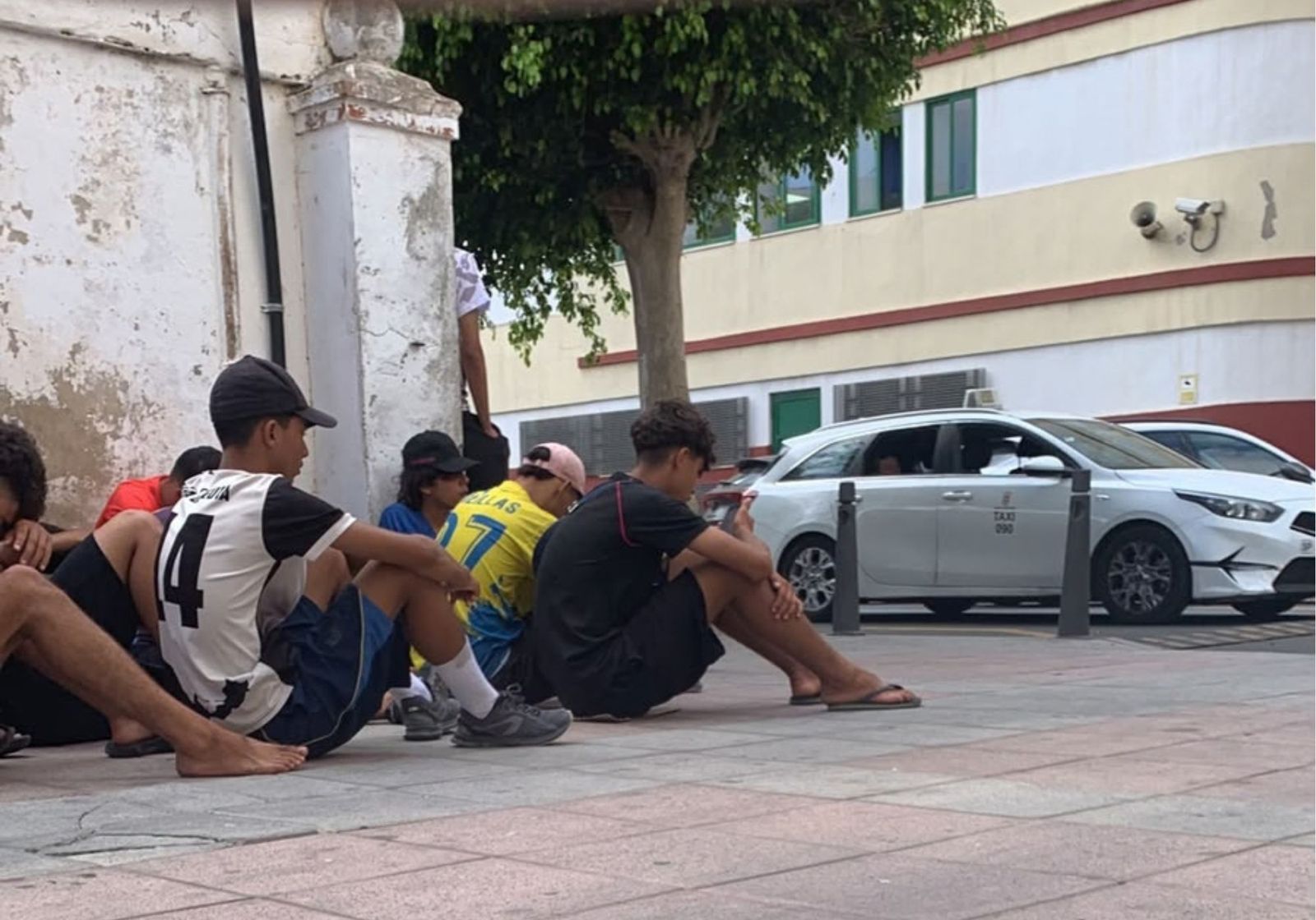 Menores migrantes en la acera de enfrente de la Jefatura de Policía.