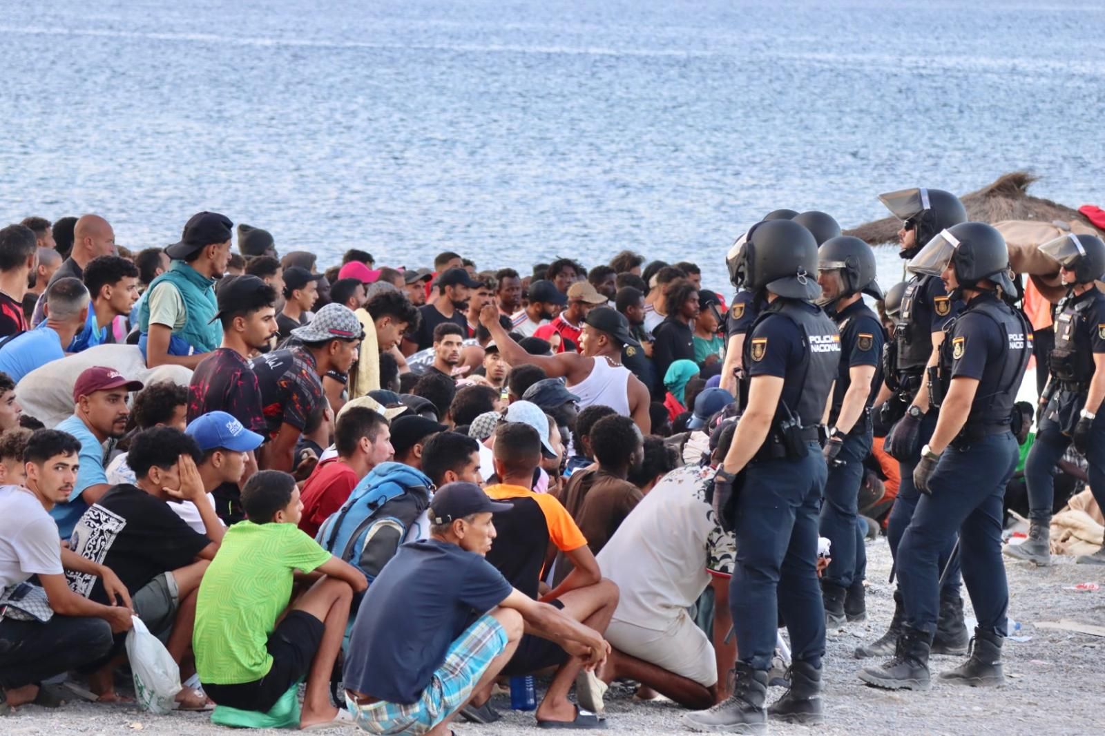 Policías nacionales controlan a centenares de migrantes en la playa del Trampolín para coordinar la entrega de comidas