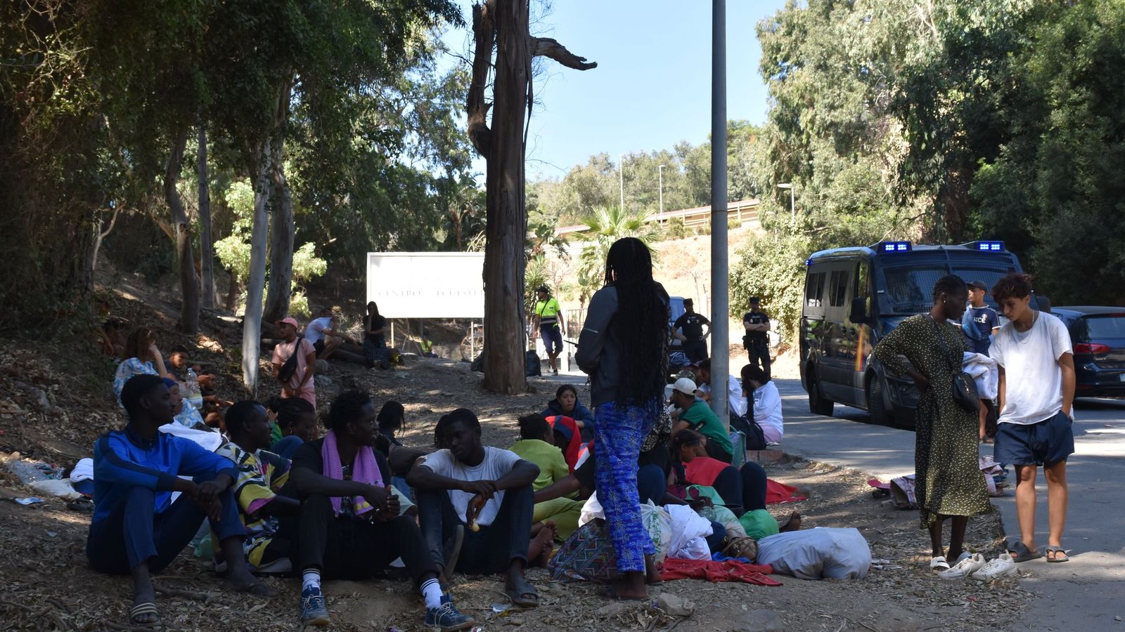 Personas migrantes sentadas en la cuneta de la carretera que conduce al CETI, este miércoles. La Policía controla el acceso al recinto para que ningún no residente pueda subir