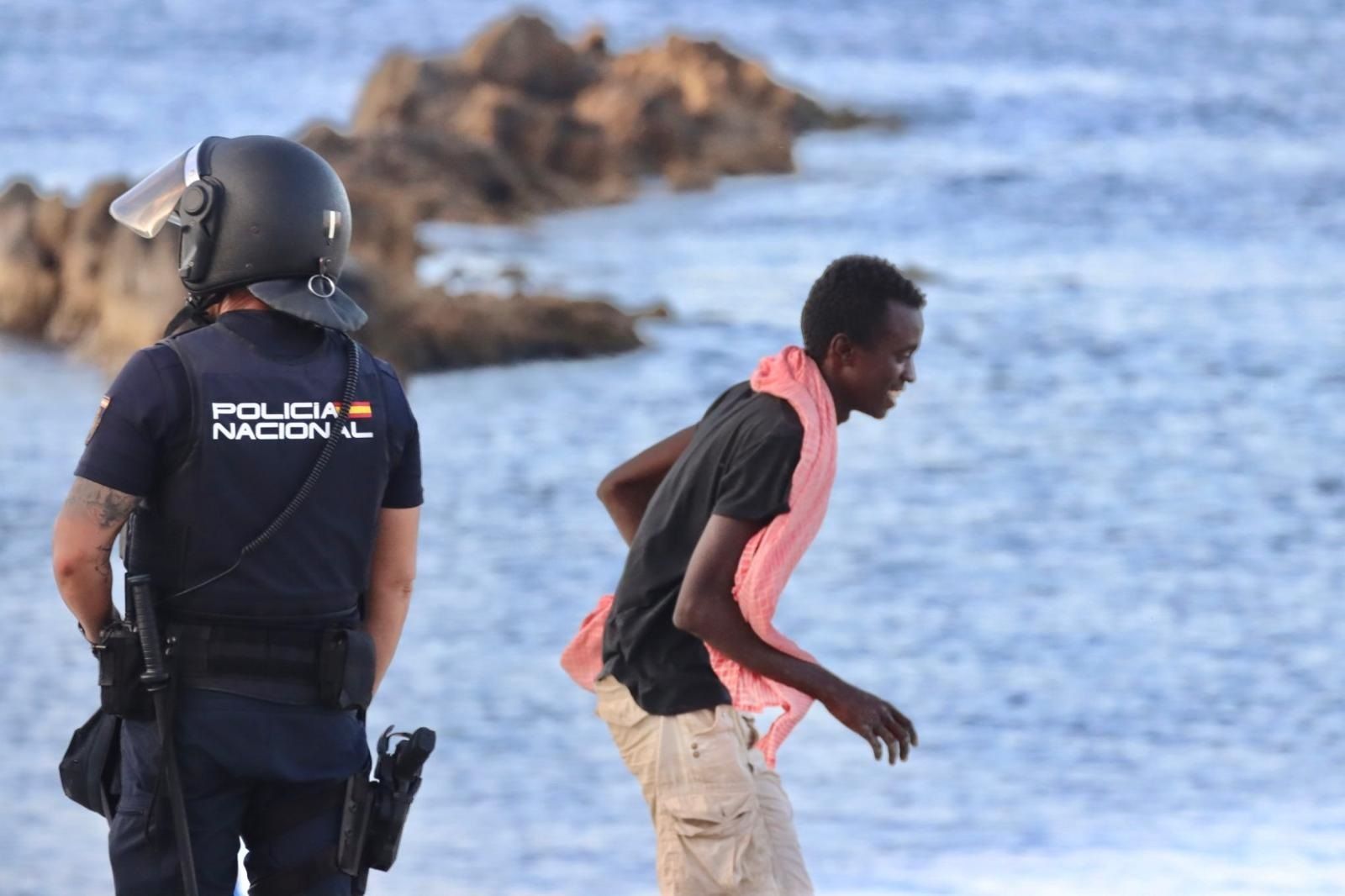 Un migrante camina por delante de un agente de la Policía Nacional