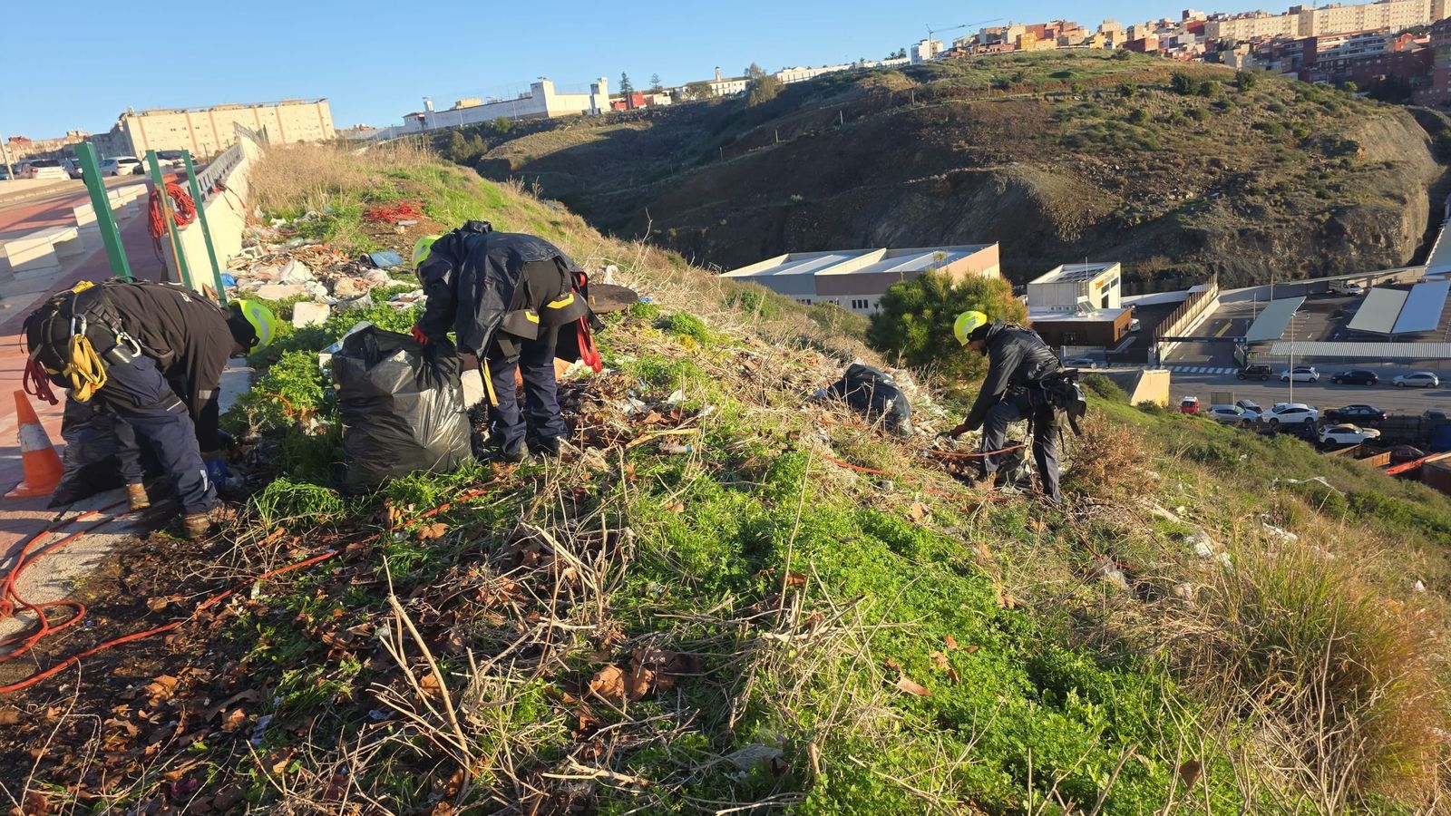 Trabajadores recogiendo basuras y escombros en un talud de Loma Colmenar