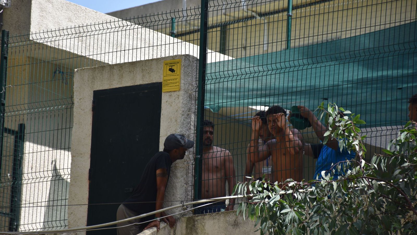Migrantes en las inmediaciones del CETI a la espera de ingresar en las instalaciones, este jueves
