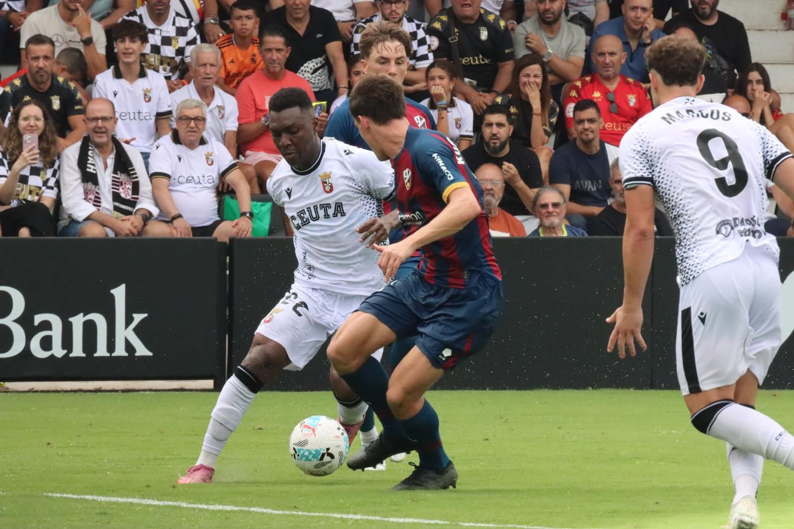 Jugada de Koné que intenta zafarse de la marca de un jugador del Huesca ante la mirada del delantero centro de la AD Ceuta FC, Marcos Fernández