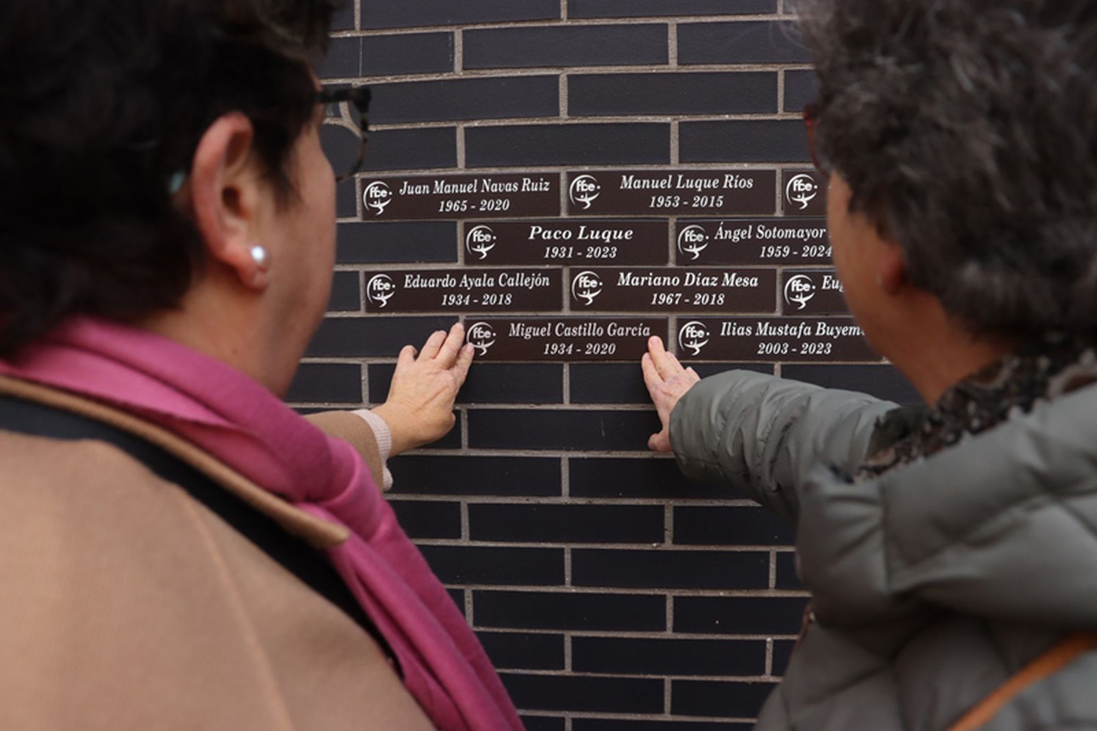 Dos ceutíes señalan la placa conmemorativa de su ser querido en el 'Muro de los Recuerdos' de la RFFCE. / FOTO RFFCE