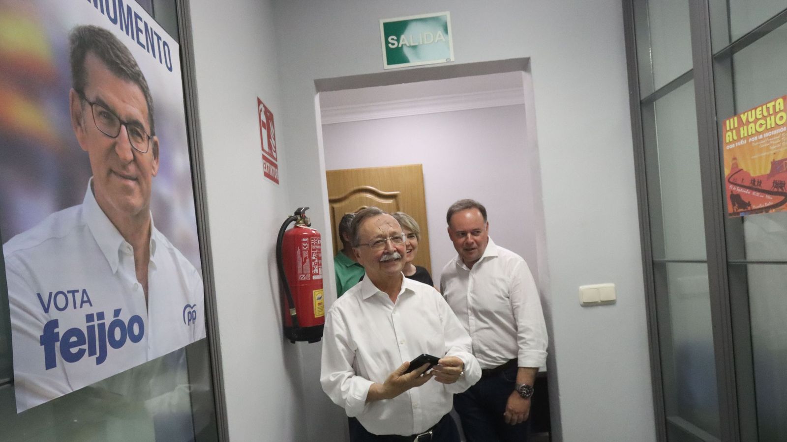 Vivas y Celaya pasando delante de un póster de Alberto Núñez Feijóo.