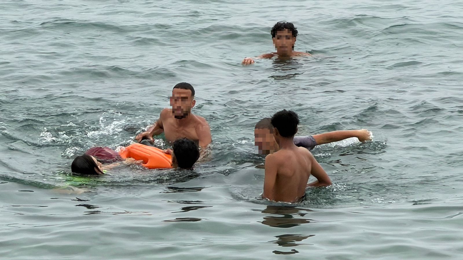 Varios migrantes ayudan a otro que acaba de llegar a nado a Ceuta