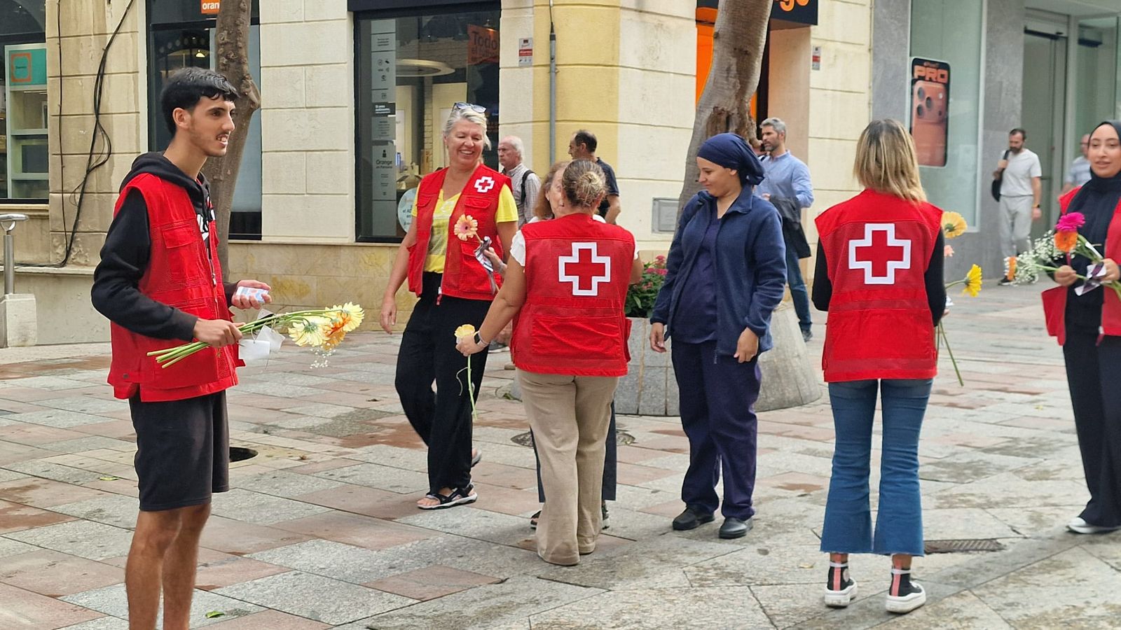 Voluntarios de Cruz Roja repartiendo flores en el Paseo del Revellín