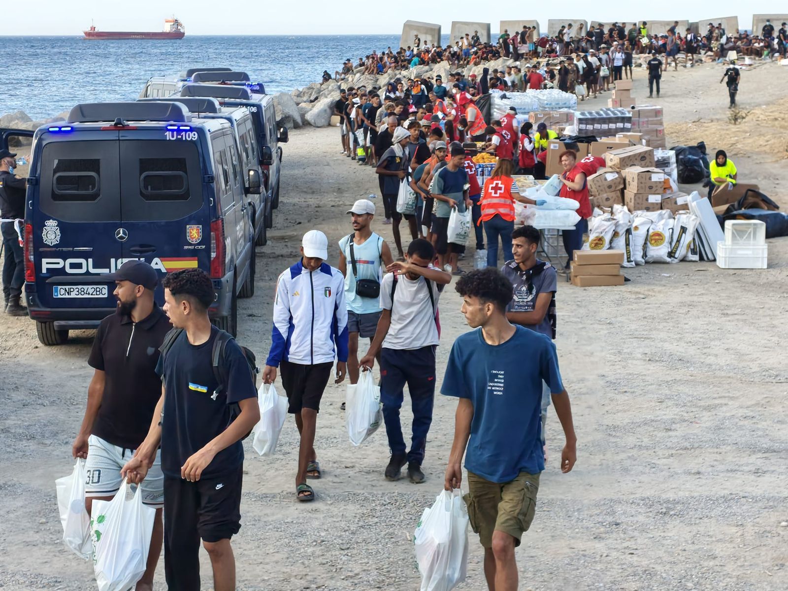 Cruz Roja reparte alimentos a los migrantes que hoy han llegado a la playa del Trampolín