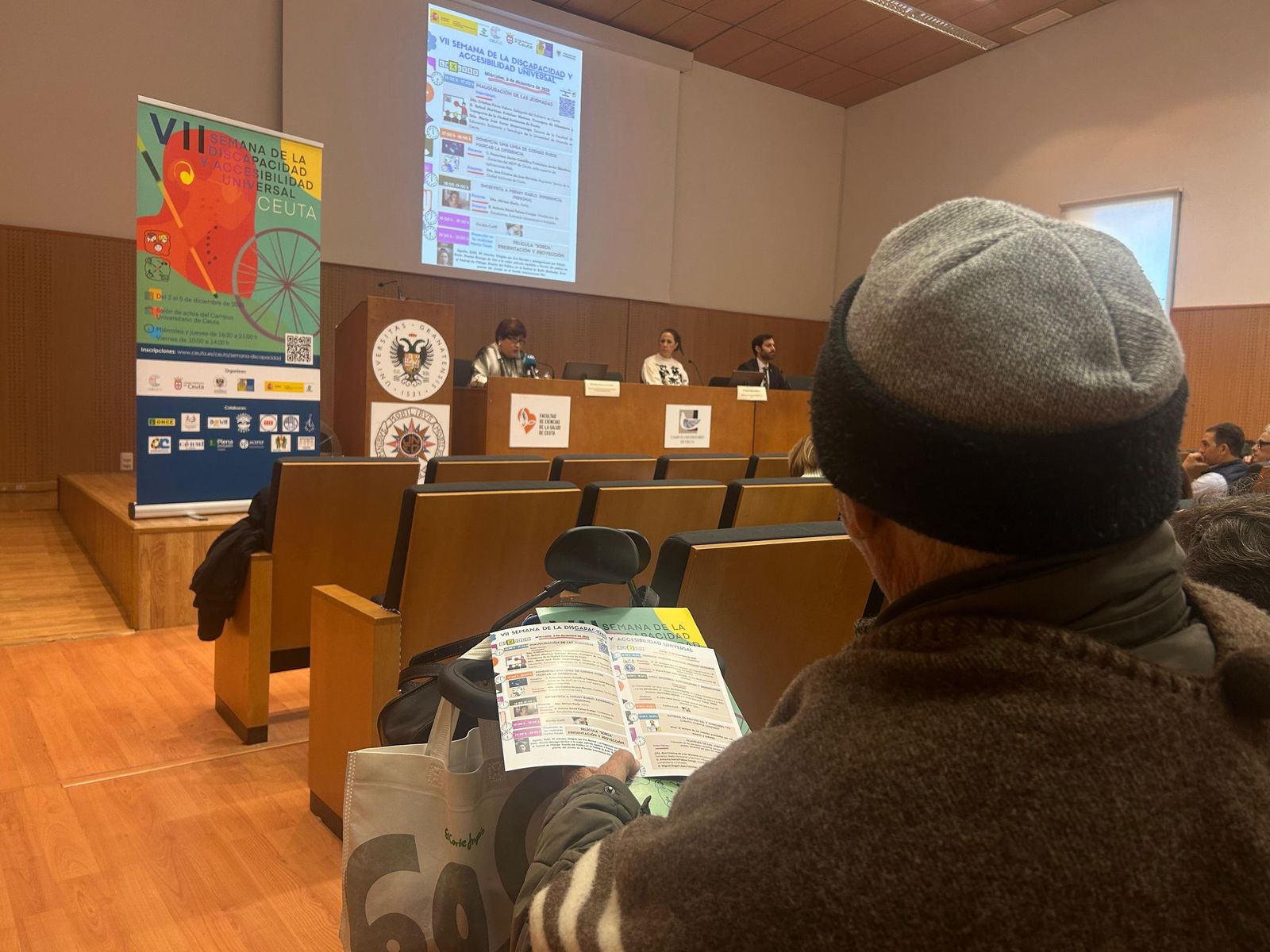 Una persona con movilidad reducida atiende a la mesa de inauguración de la VII Semana de la Discapacidad y Accesibilidad Universal de Ceuta en el Campus Universitario de la UGR