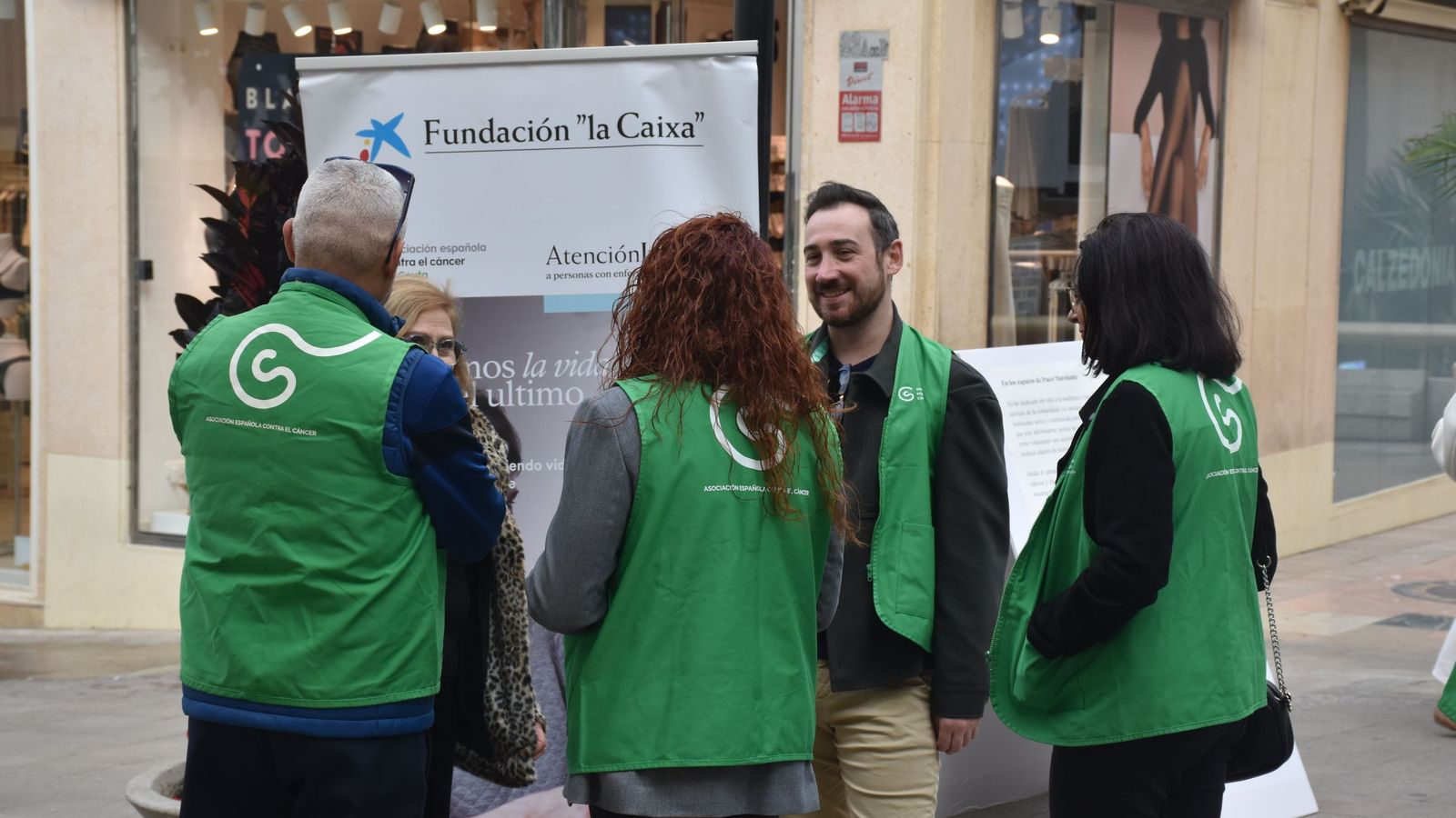 Miembros de la AECC conversan junto a la muestra 'En sus zapatos'