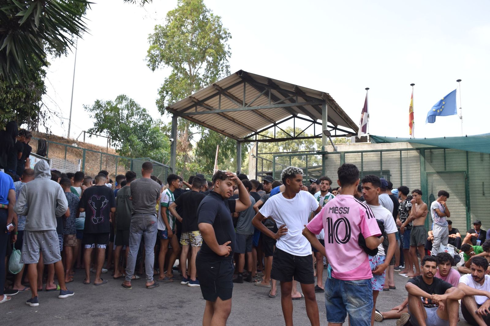 Migrantes en las inmediaciones del CETI a la espera de ingresar en las instalaciones, este jueves