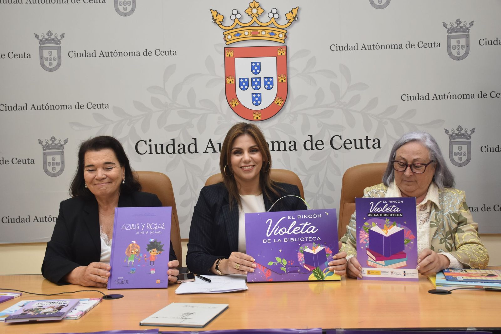 La directora general de Igualdad, Malika Al-Lal, la consejera de Servicios Sociales, Nabila Benzina, y la especialista en Igualdad, Marisa Rebolledo, posan con los maletines didácticos del proyecto ‘El rincón violeta de tu biblioteca’