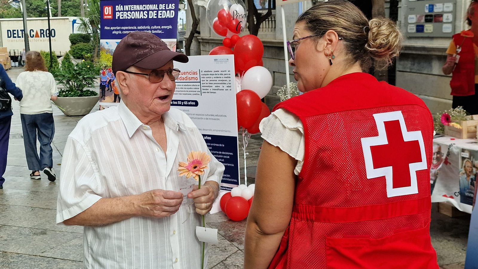 Voluntarios de4 Cruz Roja entregan flores a un mayor en el Revellín