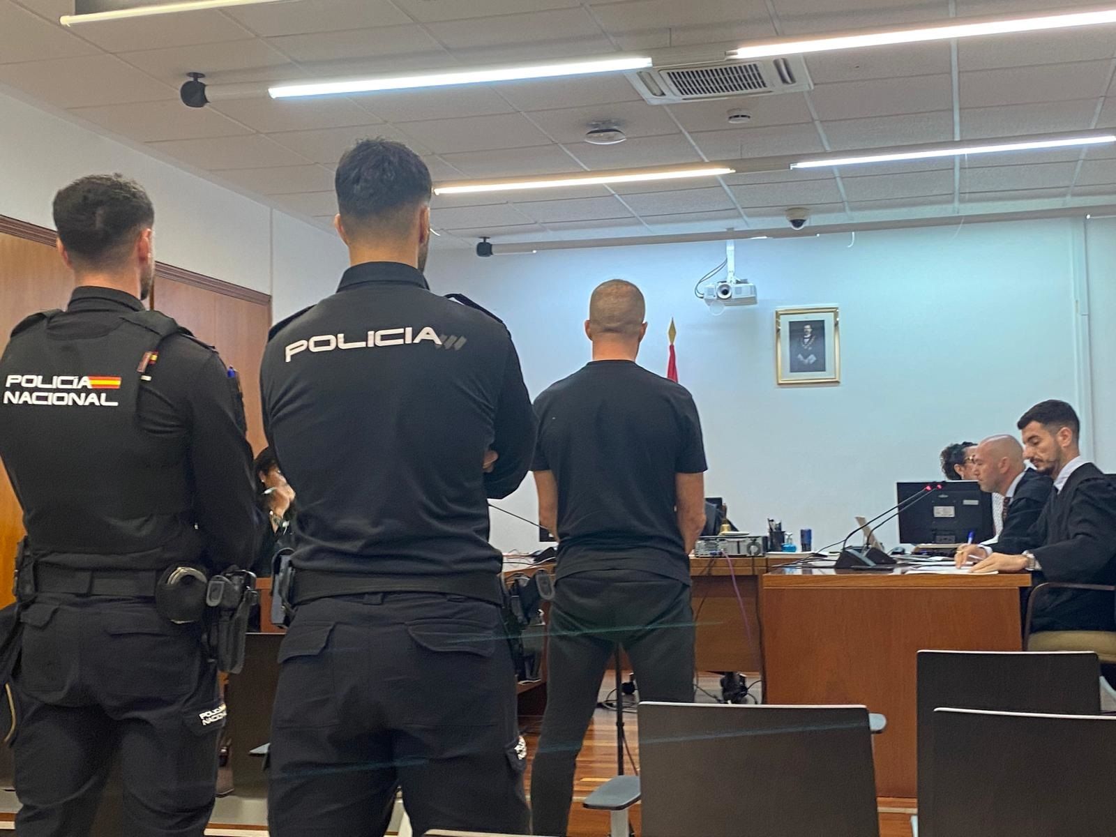 El acusado declara ante el tribunal esposado y conducido por dos policías.