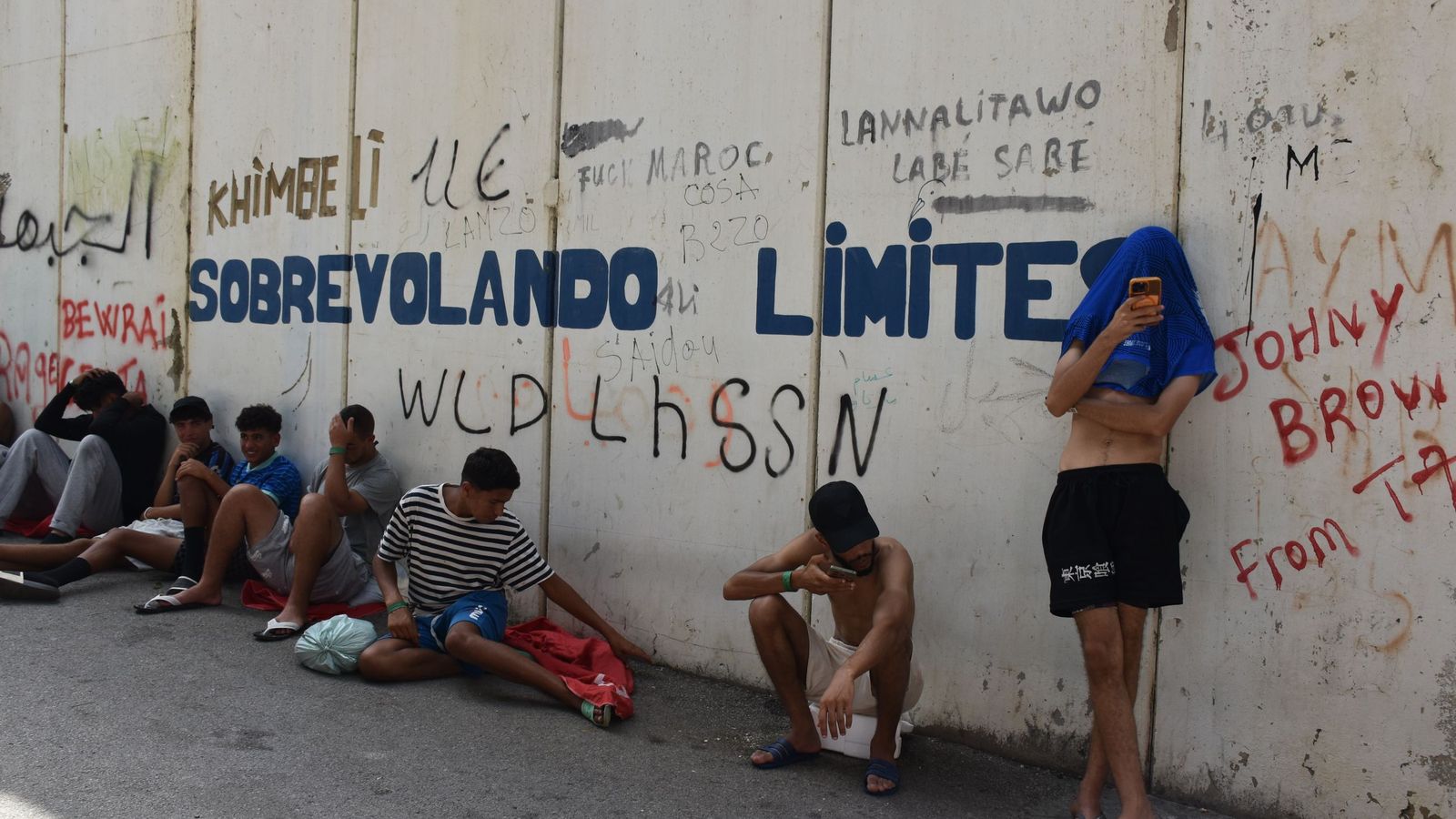 Migrantes en las inmediaciones del CETI a la espera de ingresar en las instalaciones, este jueves