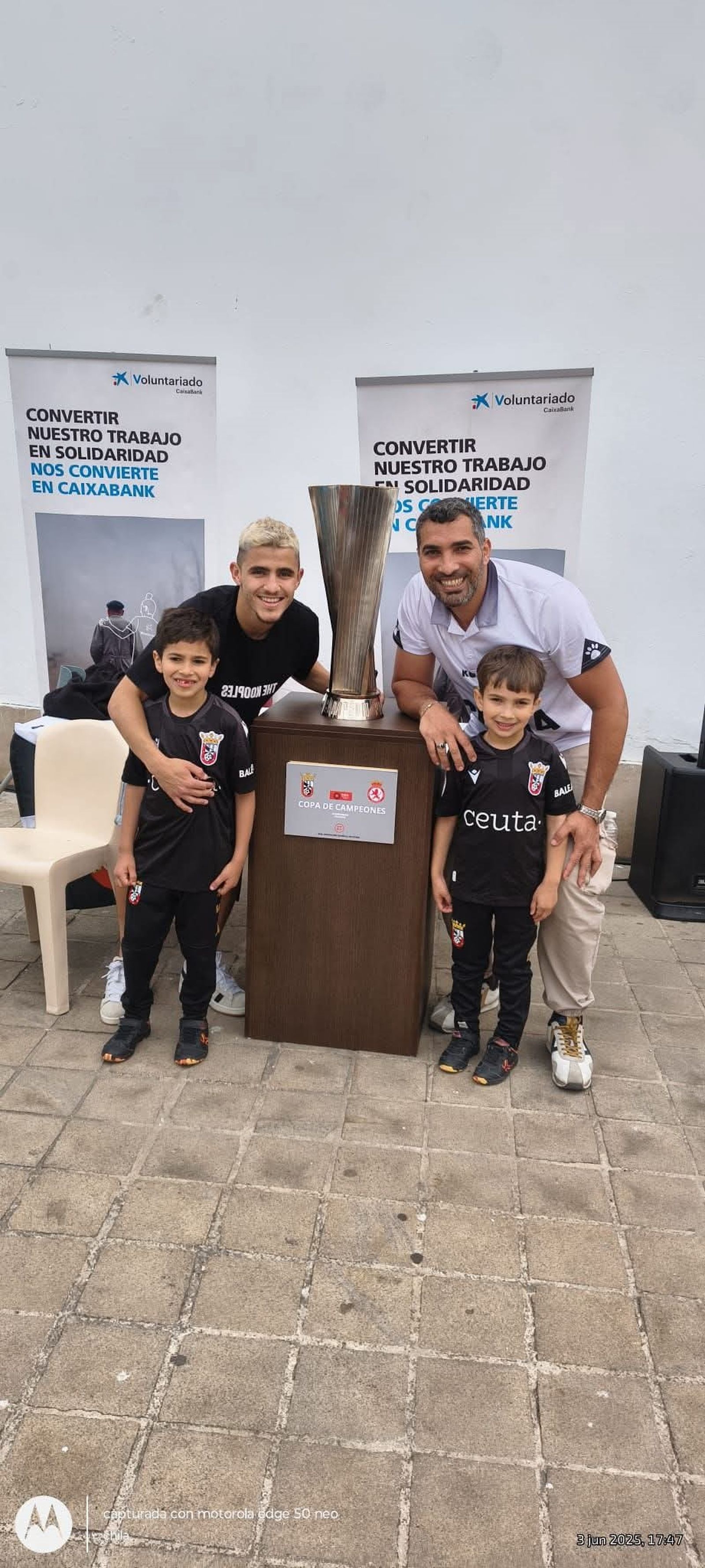 Benaisa, junto a sus hijos y el jugador de la AD Ceuta, Aisar, posando junto al trofeo tras haber conseguido quedar campeón de 1ª RFEF y lograr el ascenso a la Liga Hypermotion