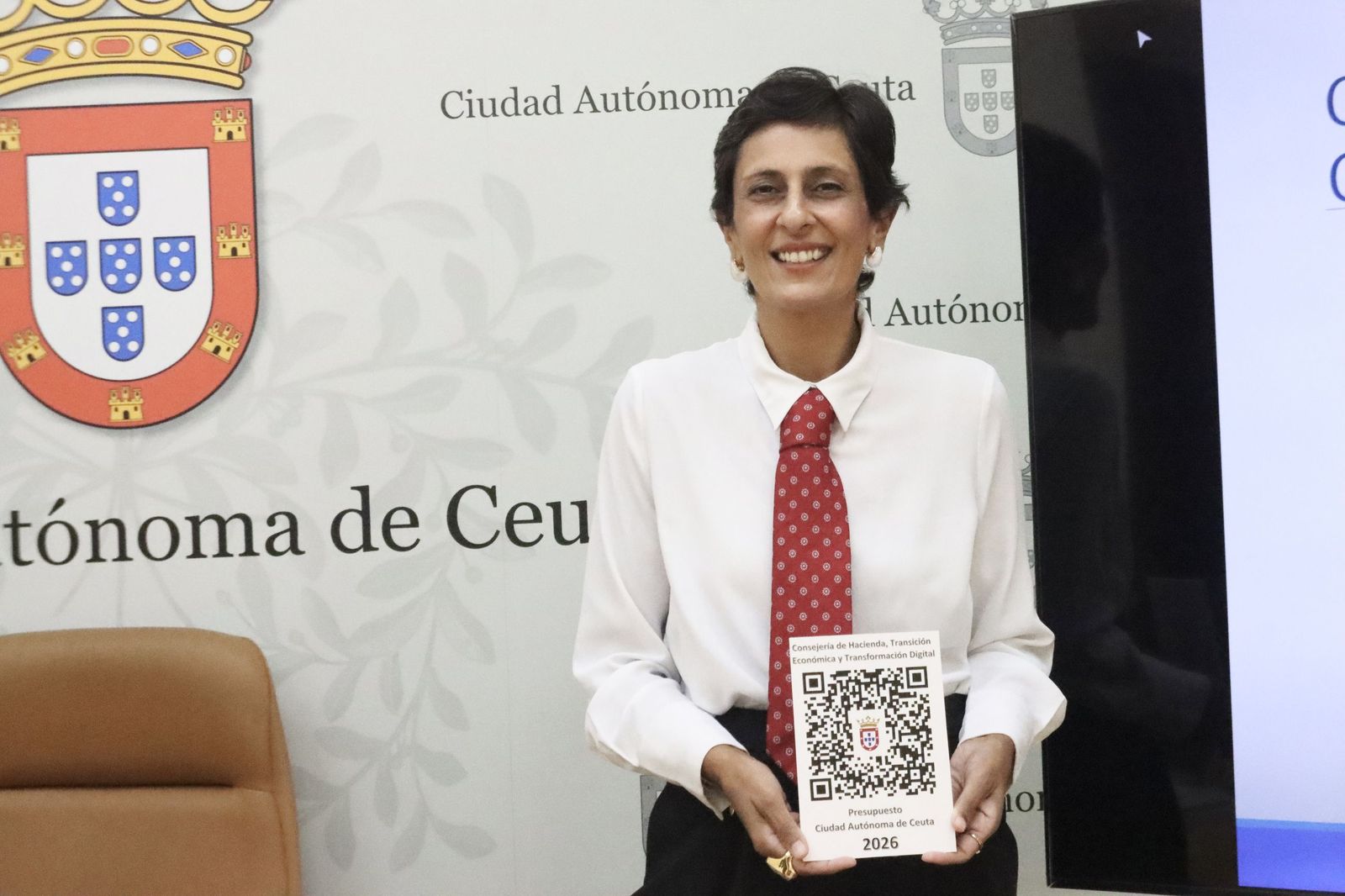 La consejera de Hacienda, Kissy Chandiramani, enseñando el QR con los Presupuestos provisionales para Ceuta 2026.