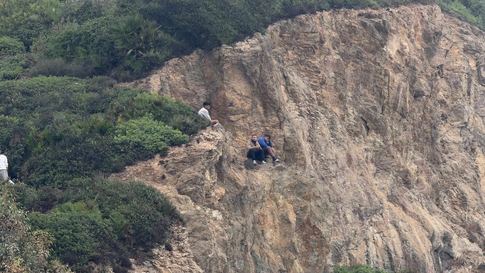 Tres migrantes en mitad del monte observando el operativo policial para desalojar el Trampolín