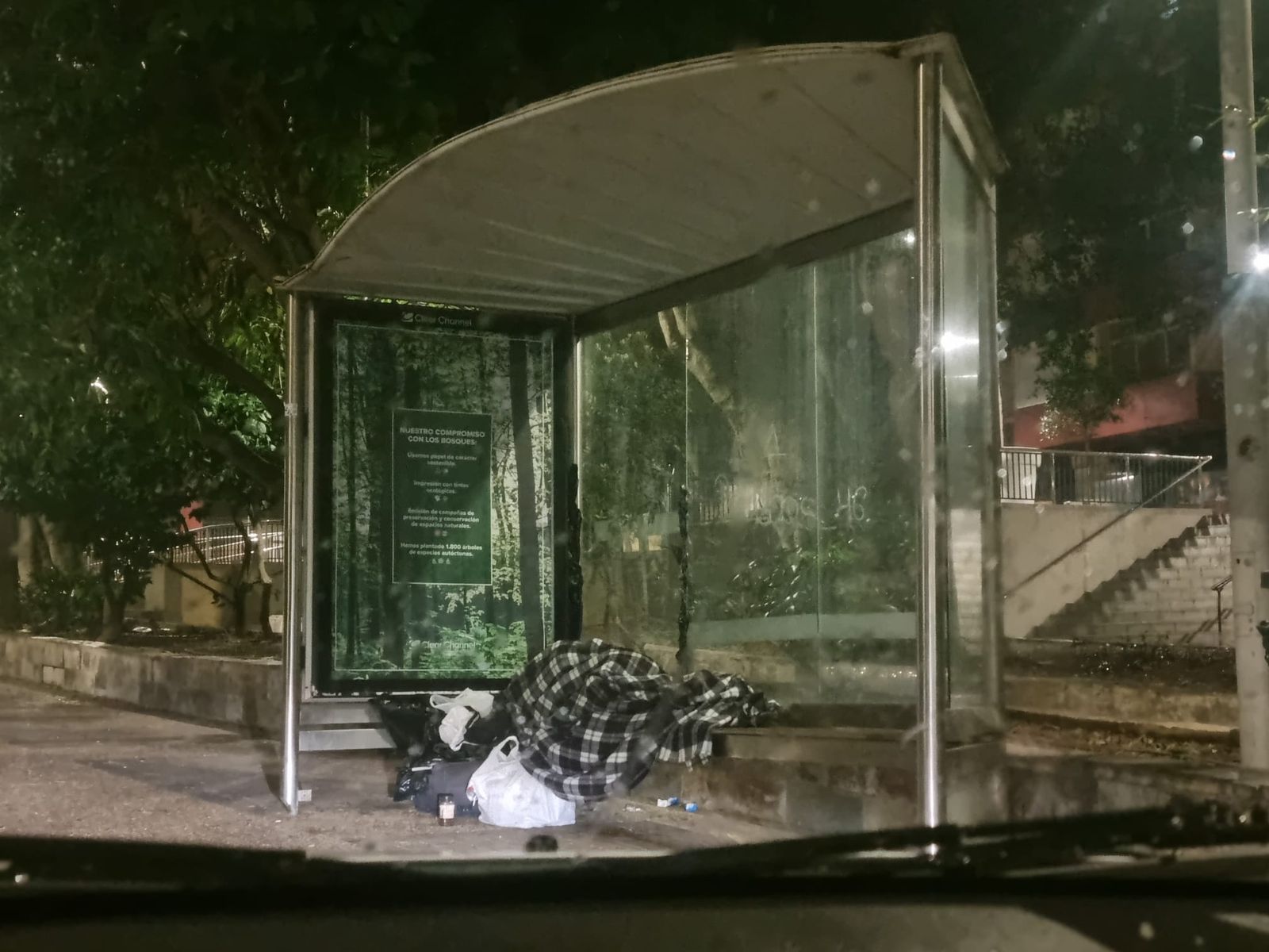 Una persona duerme bajo la marquesina de una parada de autobús