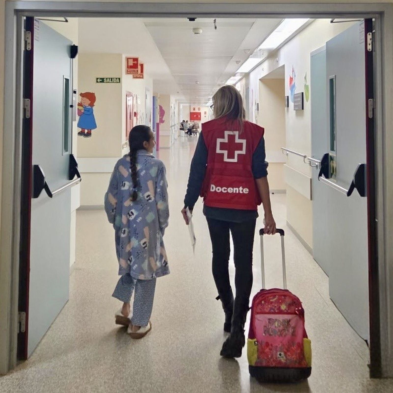 Una pequeña paciente, junto a una voluntaria de Cruz Roja